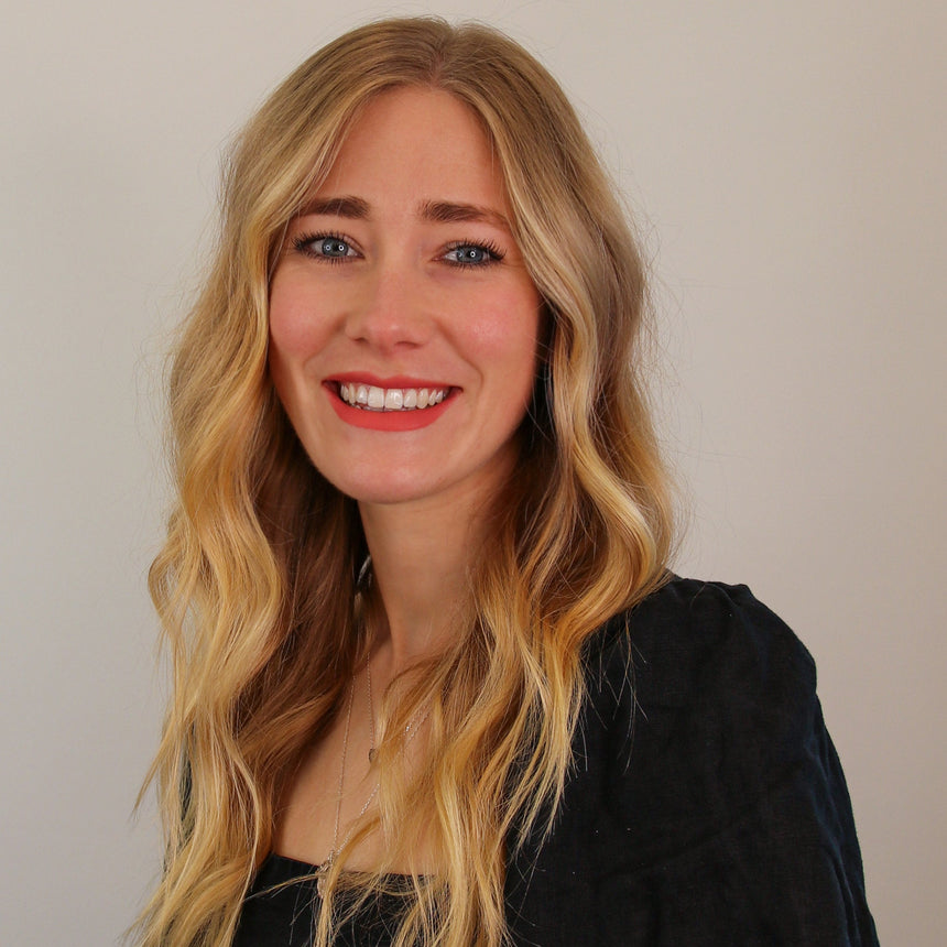 Woman with long blonde hair wearing a black top against a plain background
