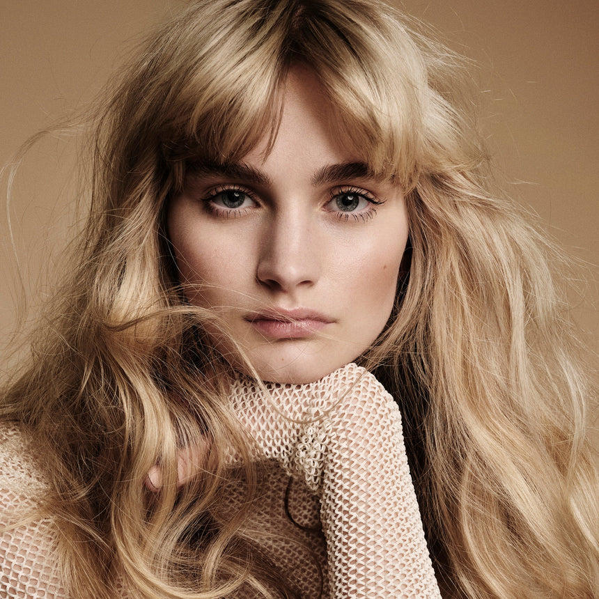 Woman with long blonde hair wearing a textured beige sweater against a neutral background