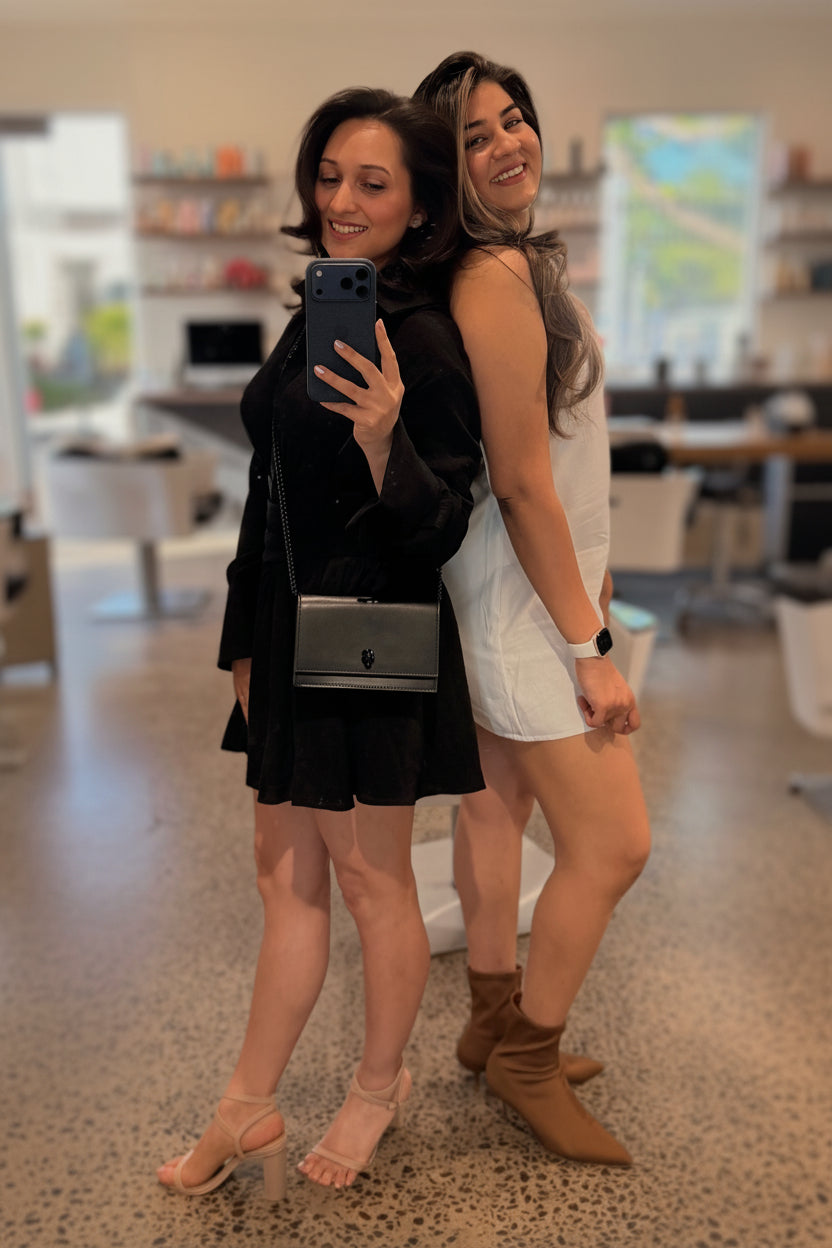Two women taking a mirror selfie in a hair salon.