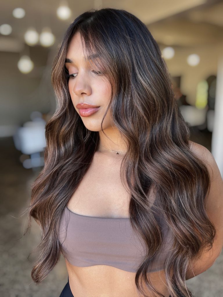 Woman with long, wavy hair wearing a brown sports bra in an indoor setting.