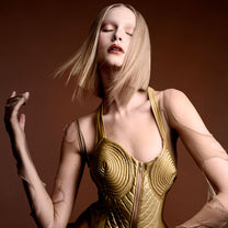 Woman wearing a gold, futuristic outfit against a brown background