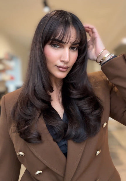 Woman with long dark hair wearing a brown coat indoors